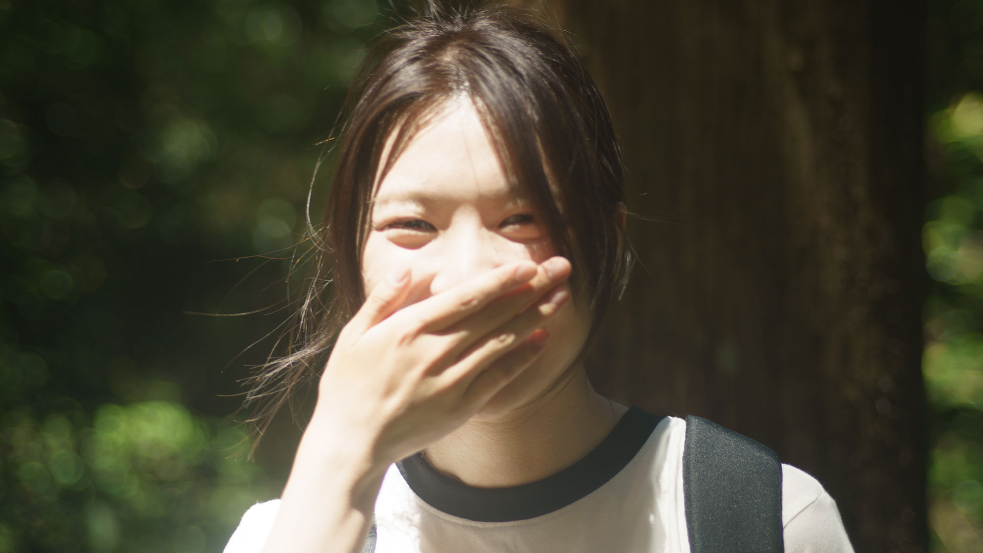 熊野の柔らかな光の中で、口元を隠して恥じらう女性の自然な笑顔。