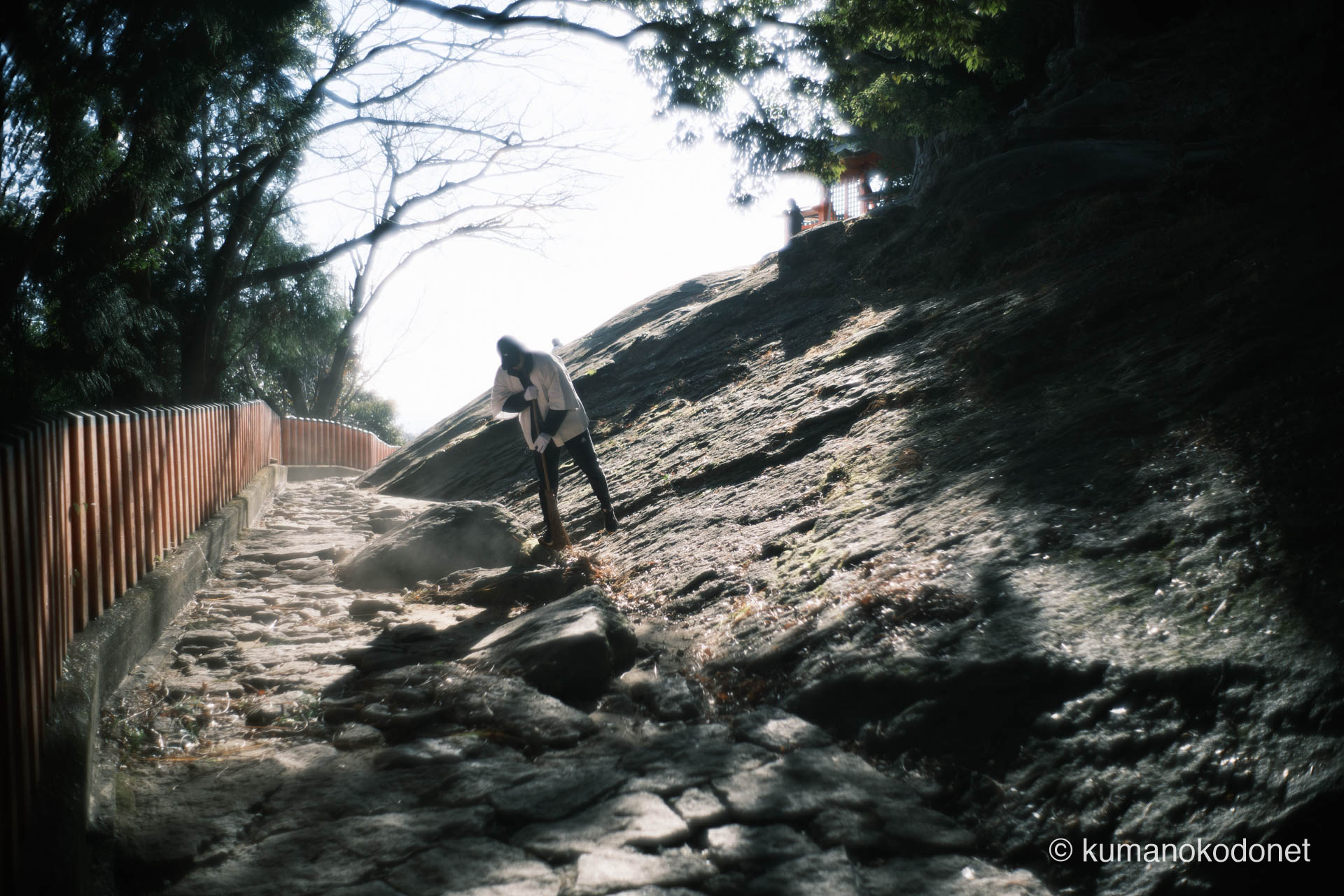 ゴトビキ岩の傍らで、竹ぼうきを手に清掃する奉仕者の姿。朝の静かな習慣。｜ Kamikura Jinja, Shingu, Wakayama ｜ FUJIFILM GFX Classic Neg. ｜ 2026