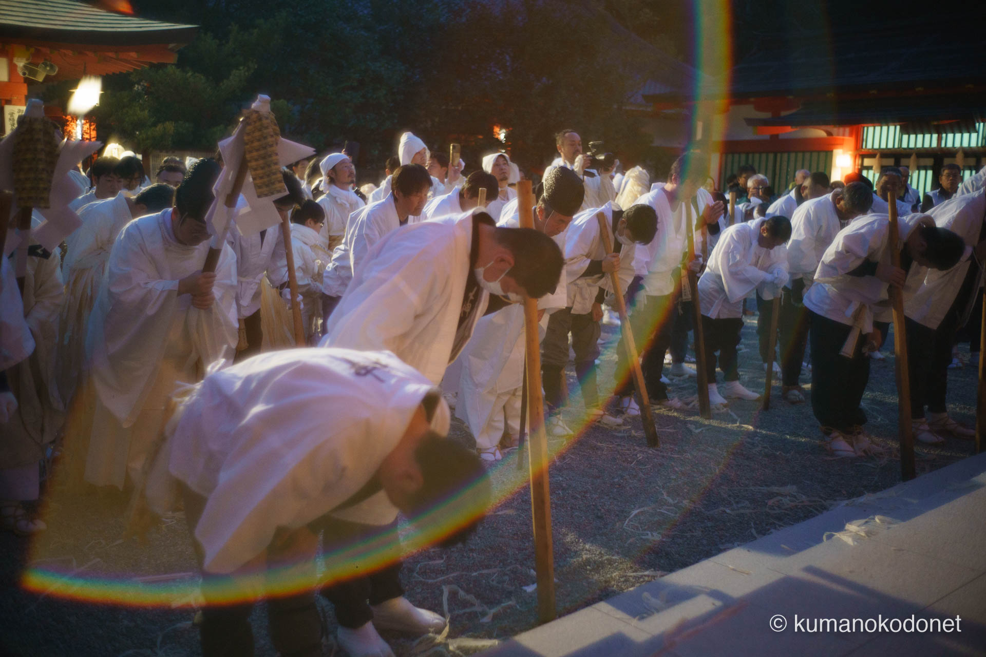 熊野速玉大社の拝殿前で、宮司を中心に神職と介釈たちが一斉に深く頭を垂れ、神事の無事を祈る情景。レンズに射し込んだ虹色の光芒が聖域を包み込み、神職の静かな祈りと介釈たちの硬派な決意が一つに溶け合う、荘厳な熱気に満ちた一コマ。 ｜ Kumano Hayatama Taisha, Shingu, Wakayama ｜ SONY α7 ｜ 2026