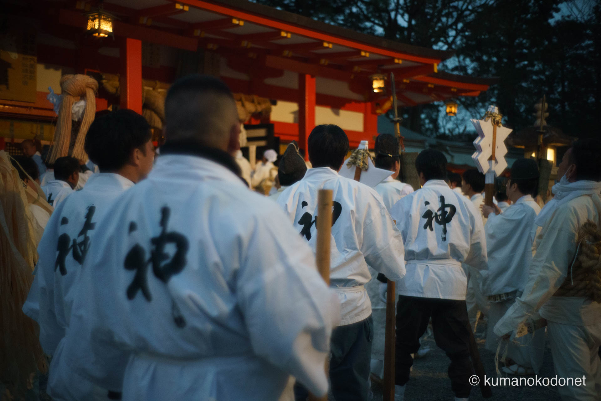 熊野速玉大社の拝殿前で、背に「神」の文字を背負い整然と並ぶ神倉青年団員たちの後ろ姿。祭りを支える介釈としての矜持を漂わせ、夕闇が深まる境内で静かに神事の時を待つ、男たちの硬派な決意が伝わる一コマ。 ｜ Kumano Hayatama Taisha, Shingu, Wakayama ｜ SONY α7 ｜ 2026