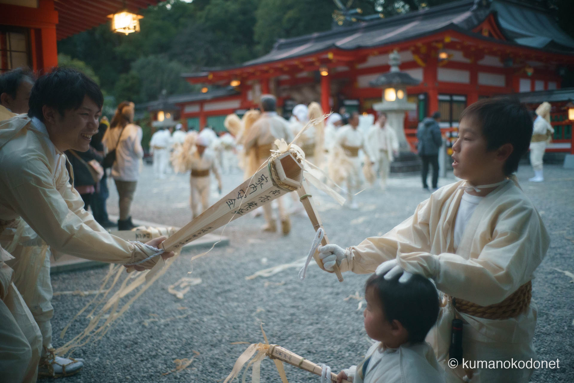 熊野速玉大社の境内で、松明を突き合わせ「頼むで〜」と声を掛け合う上り子たちの情景。20代の青年が弾ける笑顔で応え、小さな少年の松明と魂を繋ぐ、世代を超えた信頼と喜びが境内の熱気の中に溶け合う至福の一コマ。 ｜ Kumano Hayatama Taisha, Shingu, Wakayama ｜ SONY α7 ｜ 2026