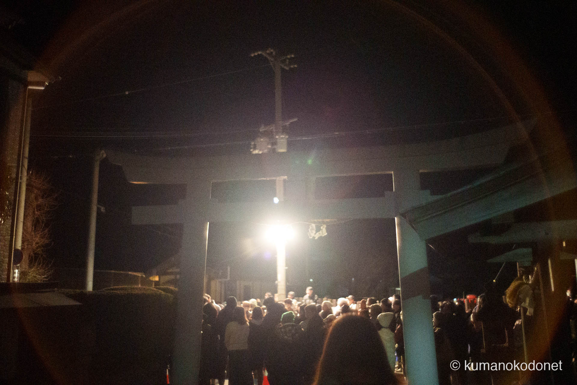 神倉山の麓、出雲大社新宮教会の鳥居越しに広がる、上り子の帰還を待つ群衆の影。夜の闇を貫く街灯の下にひしめき合う人々の期待感と、山上からの咆哮を今か今かと待ちわびる静かなる興奮が、レンズの光芒と共に夜の街に溶け込む刹那の光景。 ｜ Kamikura, Shingu, Wakayama ｜ SONY α7 ｜ 2026