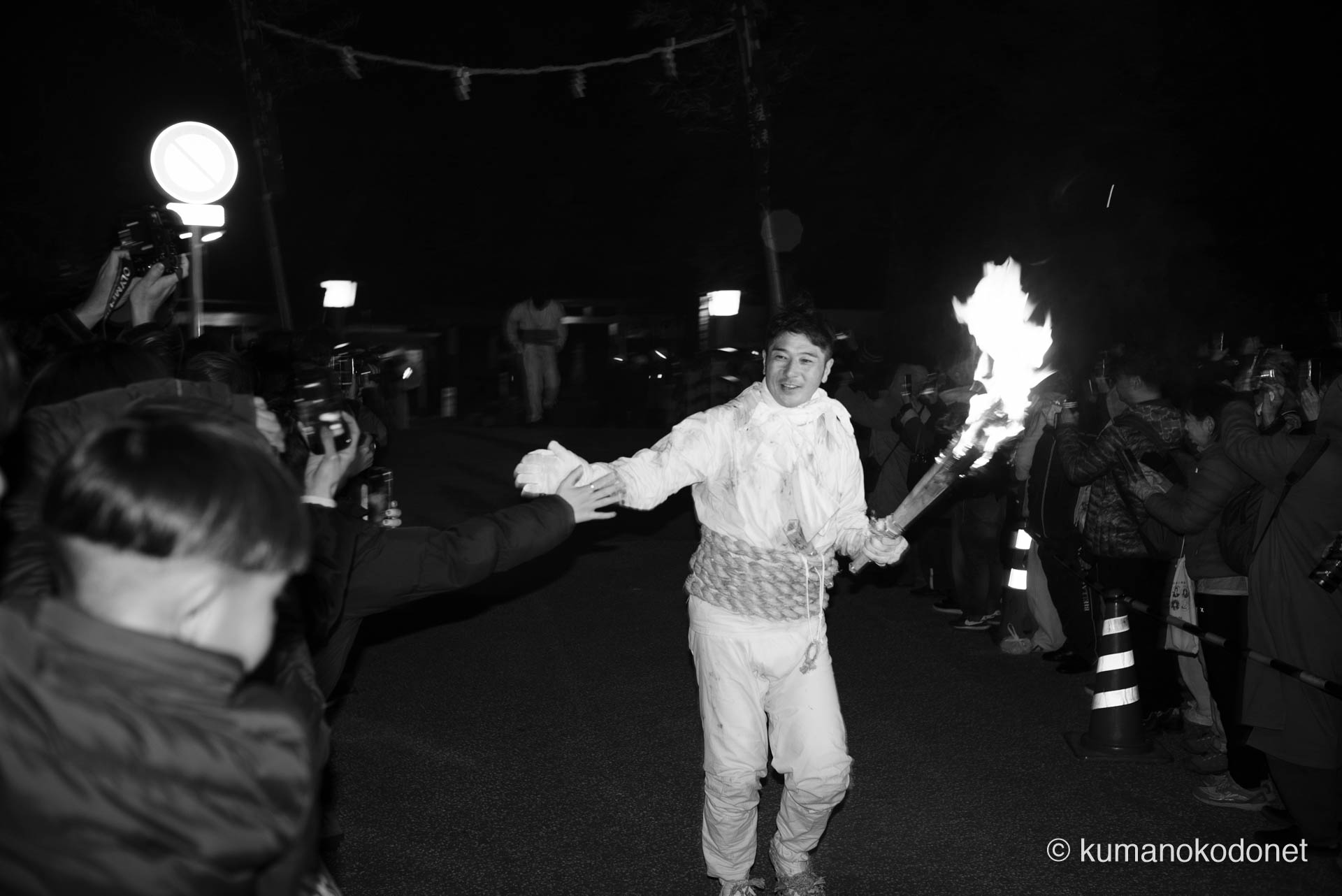 かつて幾度も一番乗りを果たした伝説を背負い、今年は悠然と神倉山を駆け下りてきた上り子の姿。沿道の観衆に手を伸ばし、新宮の街に火を届ける悦びを分かち合うその表情には、順位を超越した熟練の誇りと、神事と一体化した男の余裕がモノクロームの闇に刻まれている。 ｜ Kamikura, Shingu, Wakayama ｜ SONY α7 ｜ 2026