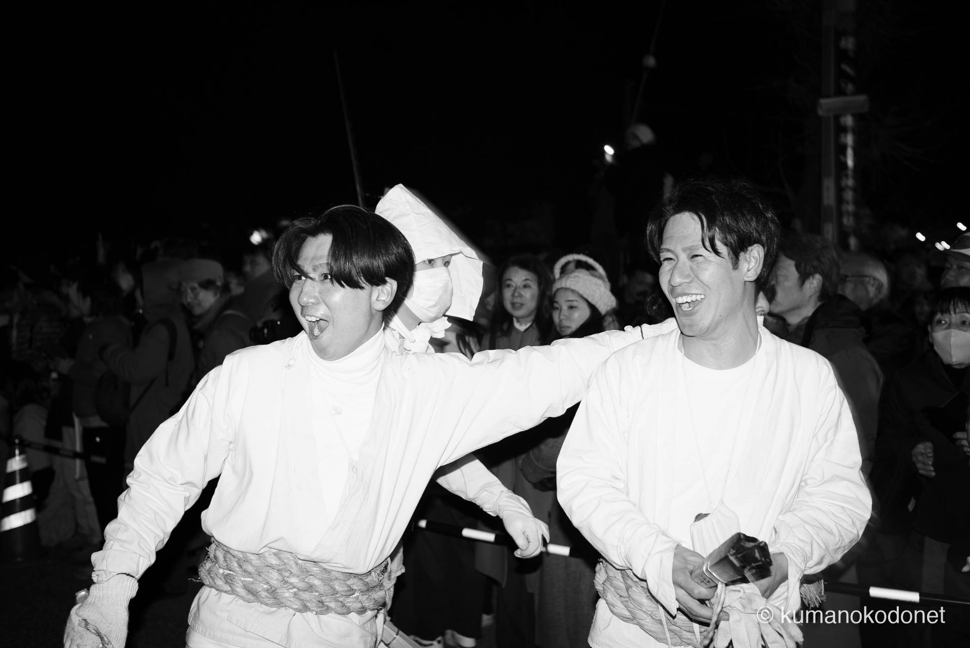 神倉山を駆け下りた直後、群衆の中に知人を見つけ、顔を綻ばせて肩を組む上り子たちの晴れやかな表情。神事の緊張から解放され、日常の絆へと回帰した瞬間の純粋な喜びが、モノクロームのコントラストの中で鮮烈に輝く、新宮の男たちの素顔。 ｜ Kamikura, Shingu, Wakayama ｜ SONY α7 ｜ 2026