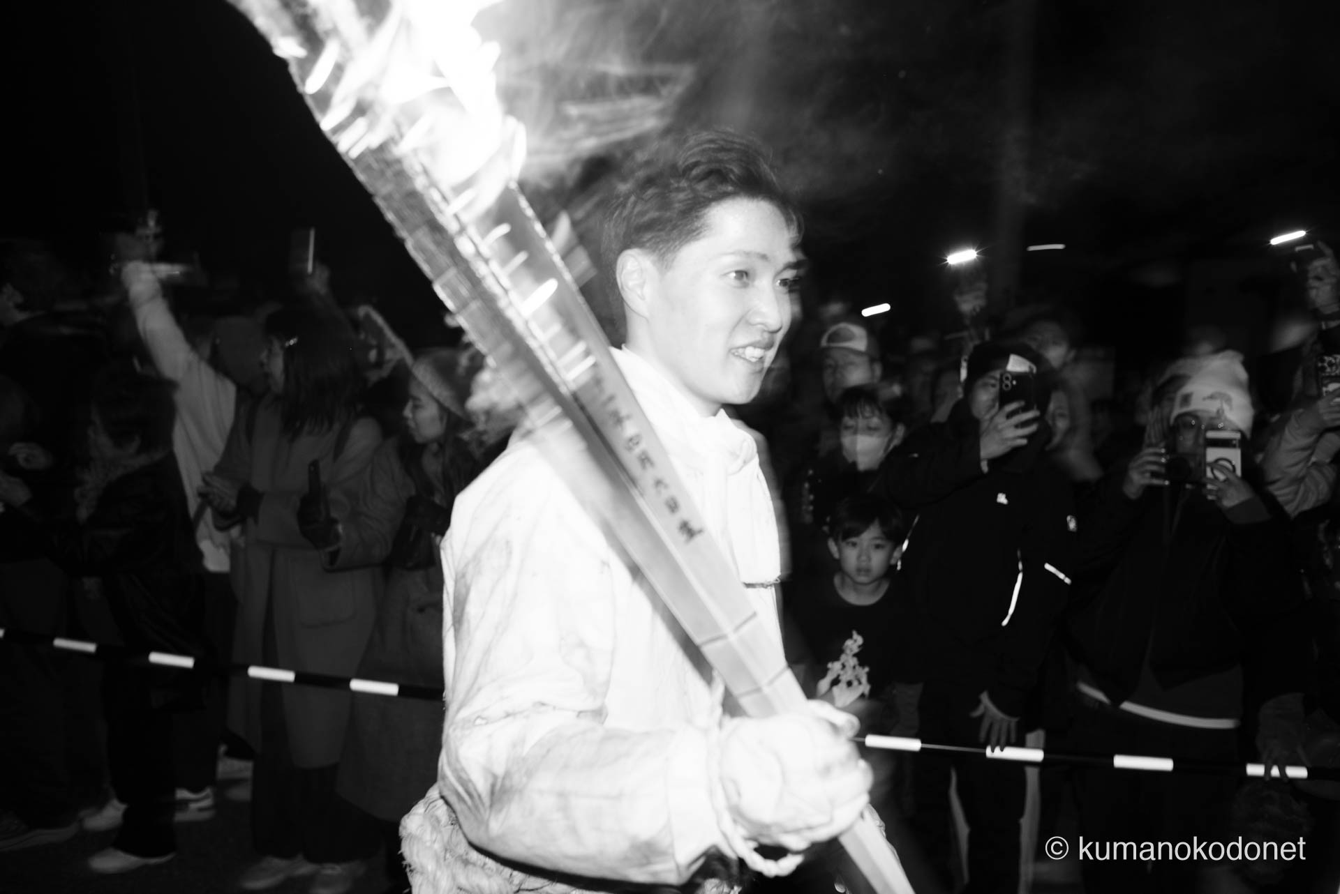 神倉山から最速で駆け下り、歓喜と興奮が最高潮に達した先頭の上り子のクローズアップ。激しく燃える松明の火影が、白装束に身を包んだ男の達成感に満ちた表情を鋭く浮き彫りにし、モノクロの階調が、新宮の夜を切り裂く熱量と静謐な神聖さを同時に描き出す。 ｜ Kamikura, Shingu, Wakayama ｜ SONY α7 ｜ 2026