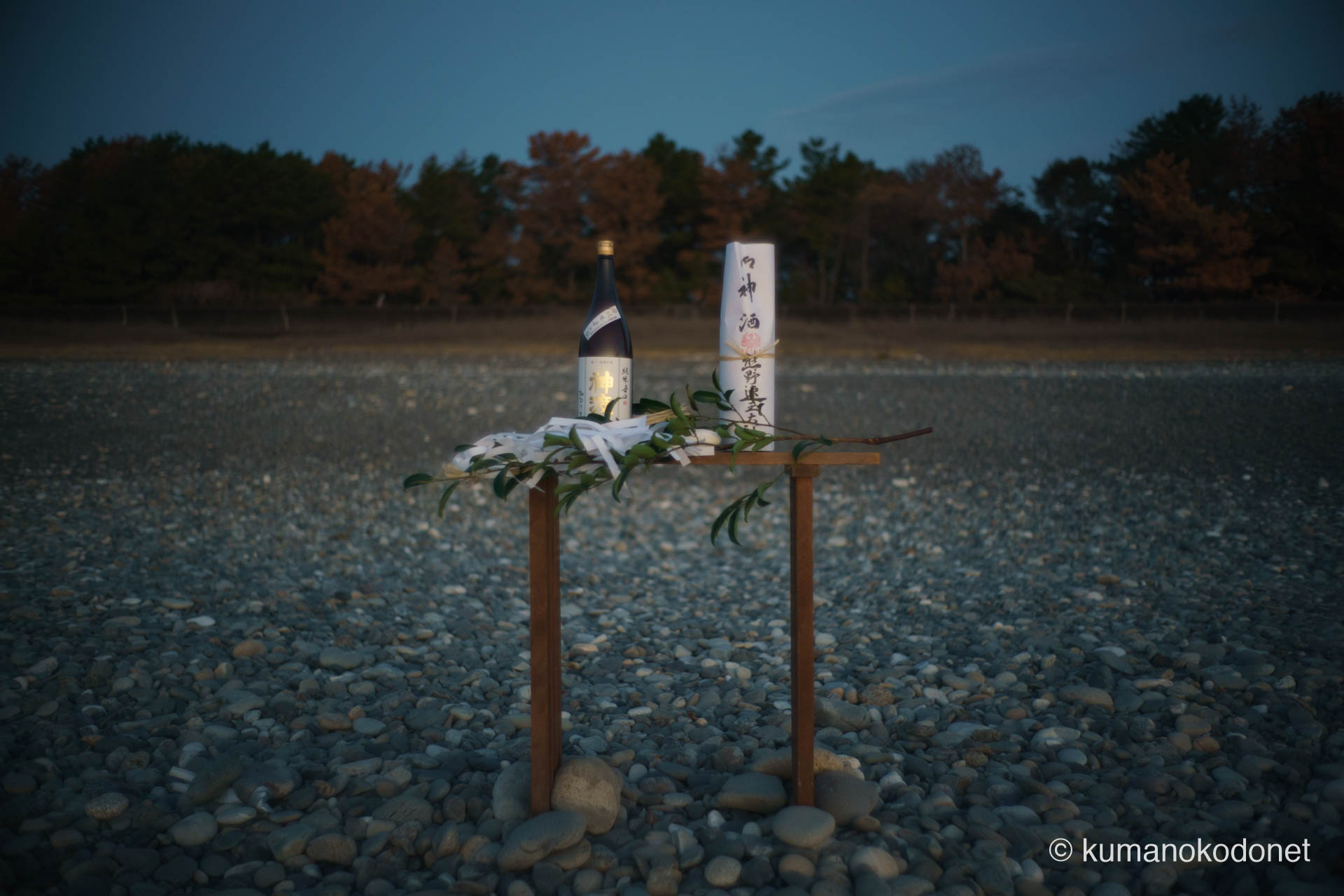 黎明の青空の下、砂利浜に設えられた祭壇と神酒