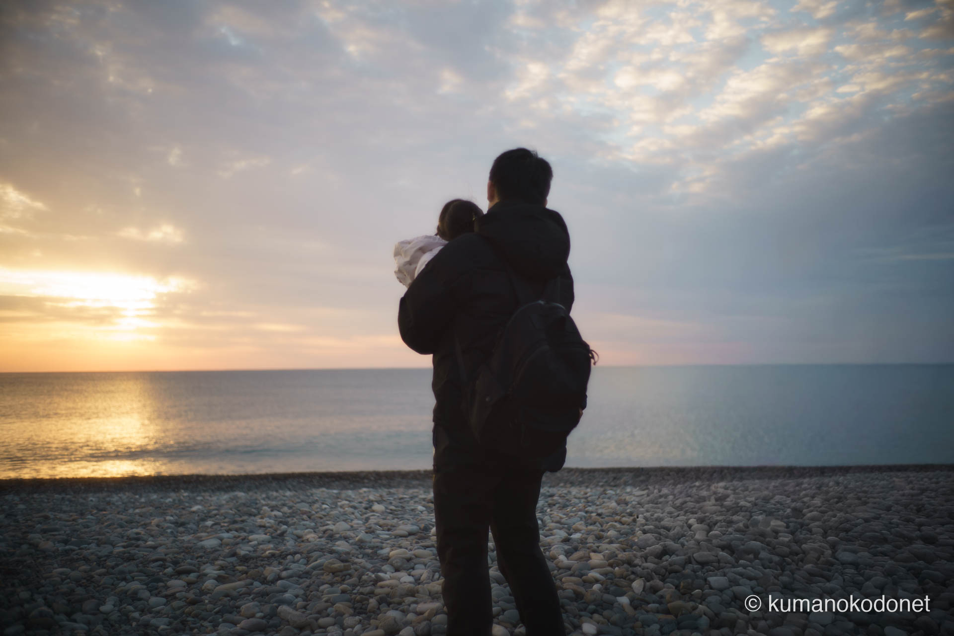 お燈祭りの「海中みそぎ」を見守り、夜明けの王子ヶ浜で子どもを抱きかかえて海を見つめる父親の後ろ姿。2026年、新宮の伝統を次世代へと繋ぐ家族の温かな記録。 ｜ Oujigahama, Shingu, Wakayama ｜ SONY α7 ｜ 2026