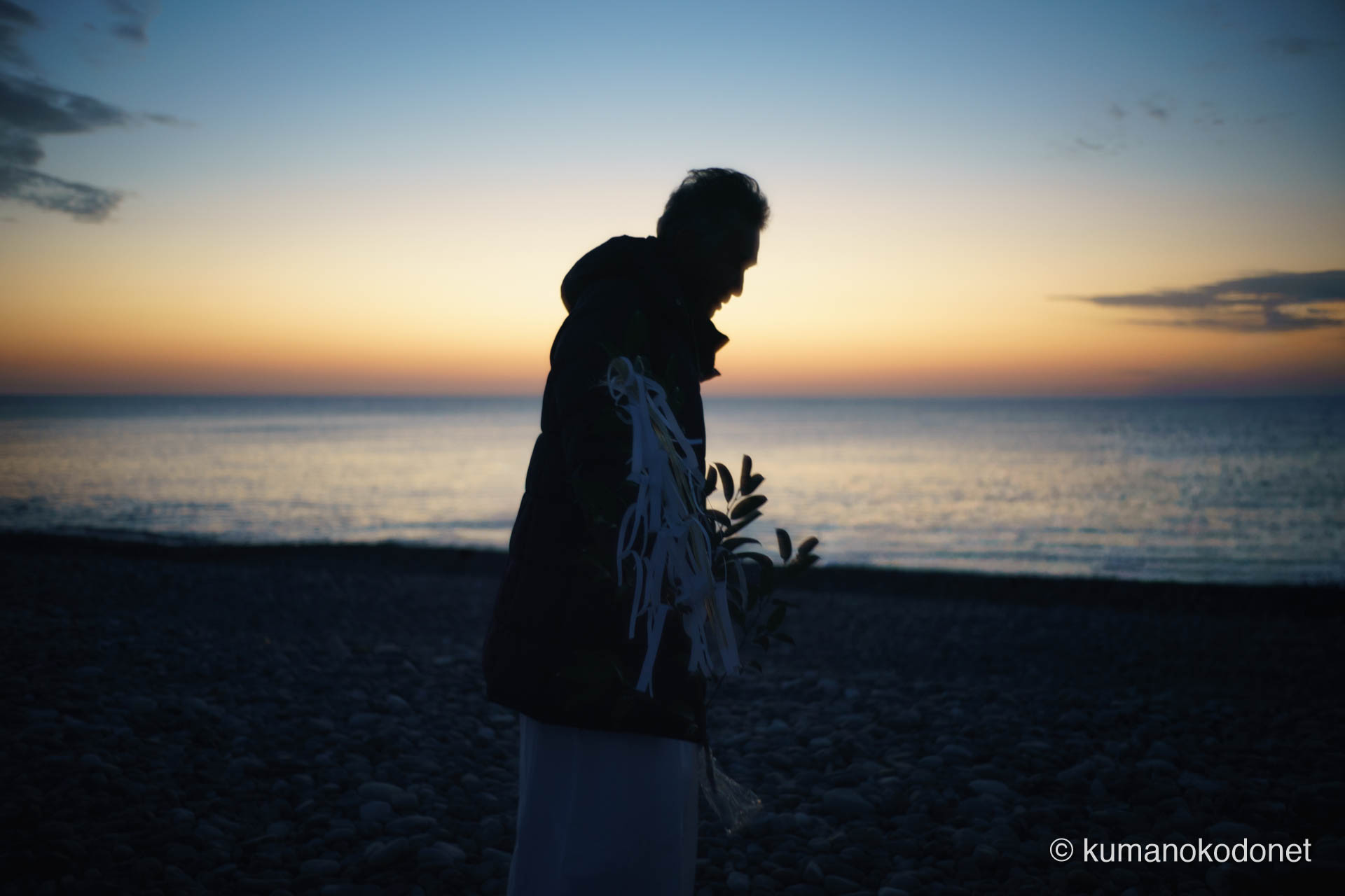 王子ヶ浜の波打ち際で、榊を手に静かに神事の準備を整える斎主。水平線には2026年の暖かい朝日の兆しが見える。 ｜ Oujigahama, Shingu, Wakayama ｜ SONY α7 ｜ 2026