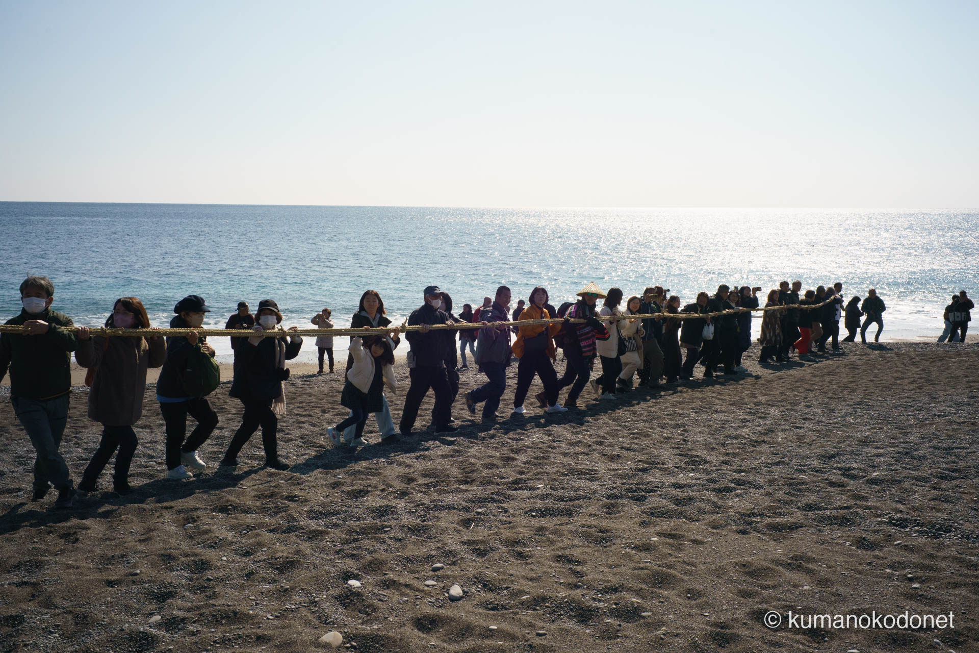 輝く水平線を背景に、砂利浜を力強く進むお綱の列。老若男女が一体となり、神聖なお綱を花の窟へと運ぶ、七里御浜ならではの開放感に満ちた一幕。| Shichirimihama Beach, Hananoiwaya Jinja, Arima, Kumano, Mie | SONY α7 | 2026