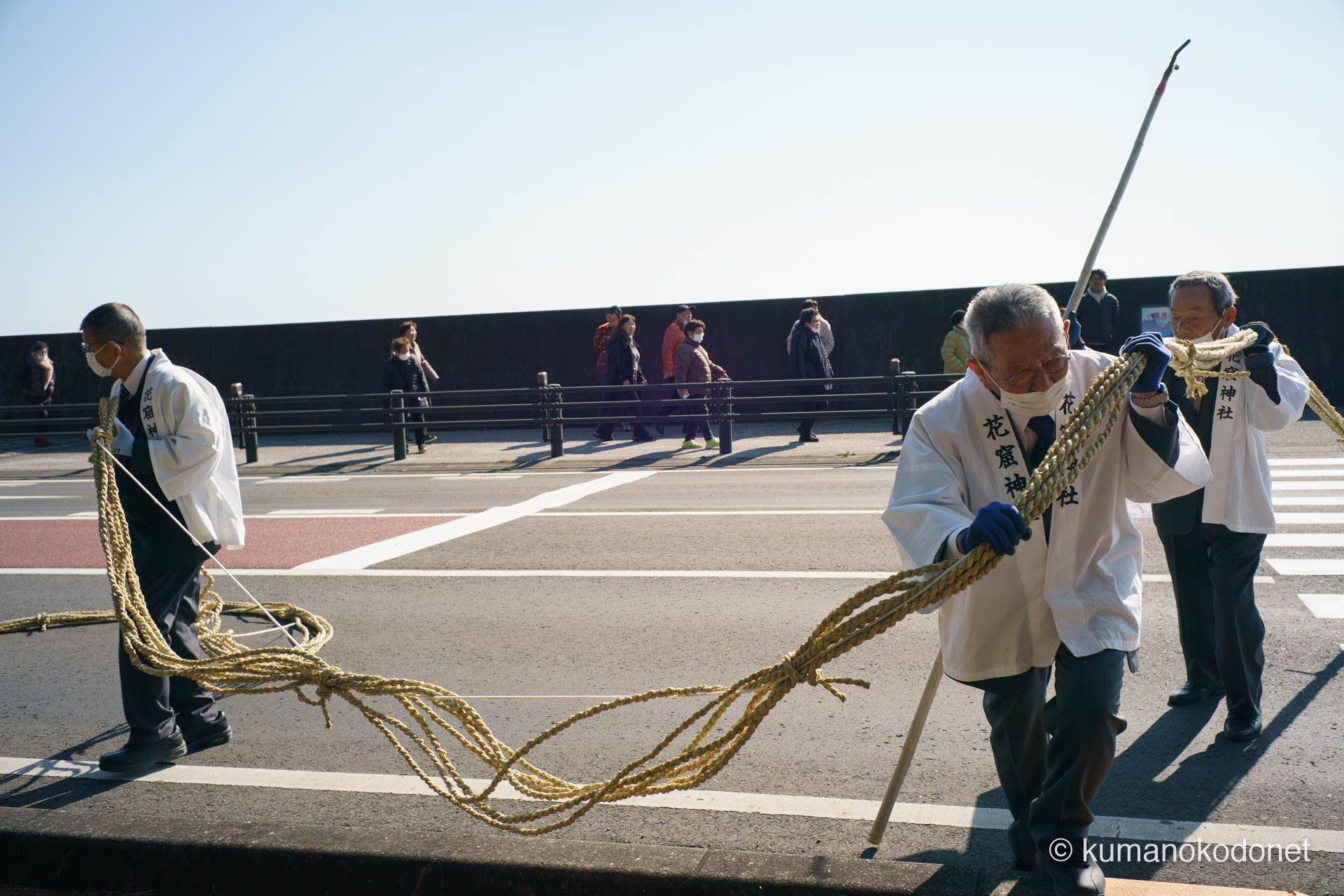 花の窟神社の例大祭にて、一時封鎖された国道42号線の横断歩道を渡り、巨大なお綱を力強く引き寄せる白装束の氏子たちの記録。七里御浜から神域へと綱を繋ぐため、アスファルトの上で懸命に力を合わせる2026年神事の決定的一枚。| Hananoiwaya Jinja, Arima, Kumano, Mie | SONY α7 | 2026