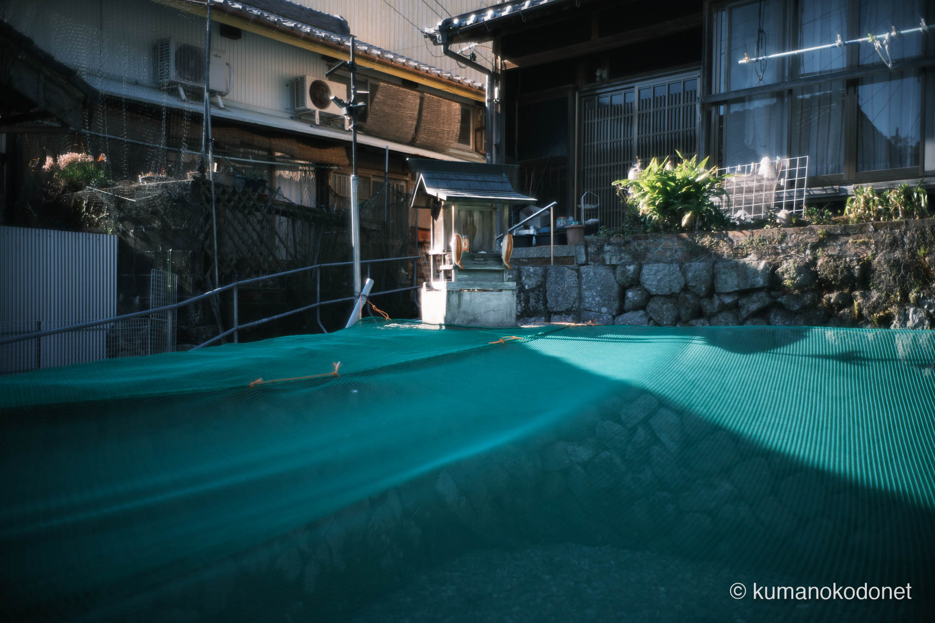石積みの上に鎮座する「にらくら祭り」の神様。緑の防球ネットが張られた独特の祭祀空間を静かに記録。｜ Kuki, Owase, Mie ｜ FUJIFILM GFX Classic Neg. ｜ 2026