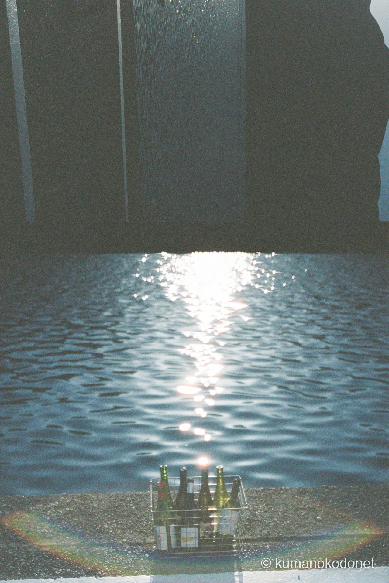 ガードレールのない岸壁に置かれたワインボトル。眩しいほどに煌めく九鬼の海と、足元に広がる光の粒子を記録する。｜ Kuki, Owase, Mie ｜ Kodak Portra 400 ｜ 2026