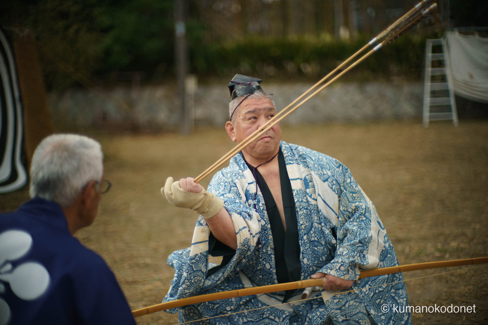 二本の矢を高く掲げ、真っ直ぐに見つめる射手の横顔。合計4回行われる奉納のうち、一射一射に魂を込め、道具と自己を一体化させる伝統儀式の厳かさを捉えたポートレート。| Tenma Tenjinja, Nachikatsuura, Wakayama | SONY α7 | 2026