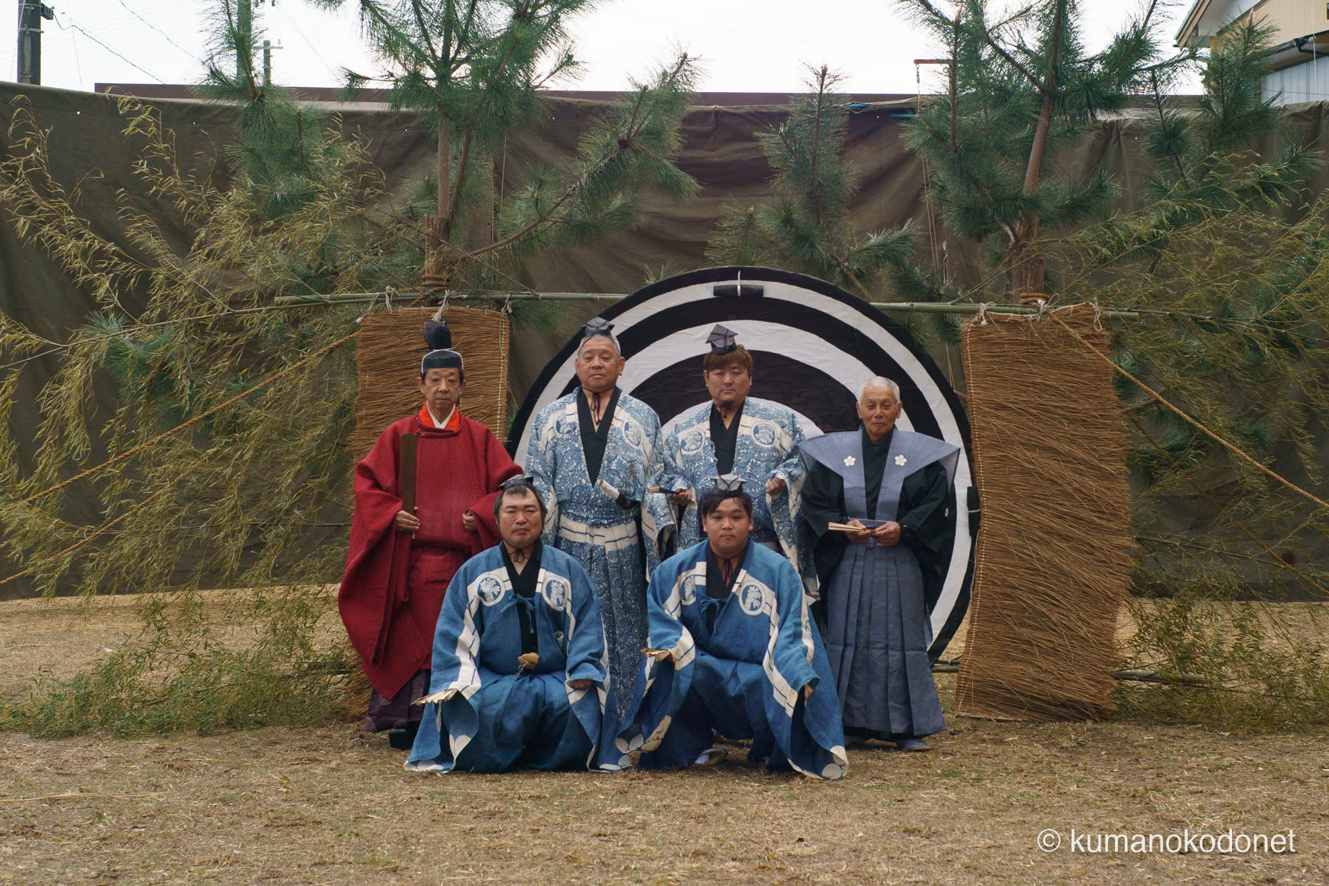 天満天神社の弓行事(ゆみぎょうじ)を前に、直径約20cmの的の前に集結した高橋正樹宮司と四人の射手(森谷正直さん、石橋隼人さん、中根拓さん、竹内虹太さん)、そして祭事役員。伝統の青い装束と赤い宮司の装束が、弓を射る神聖な舞台で一堂に会する歴史的な一枚。 | Tenma Tenjinja, Nachikatsuura, Wakayama | SONY α7 | 2026