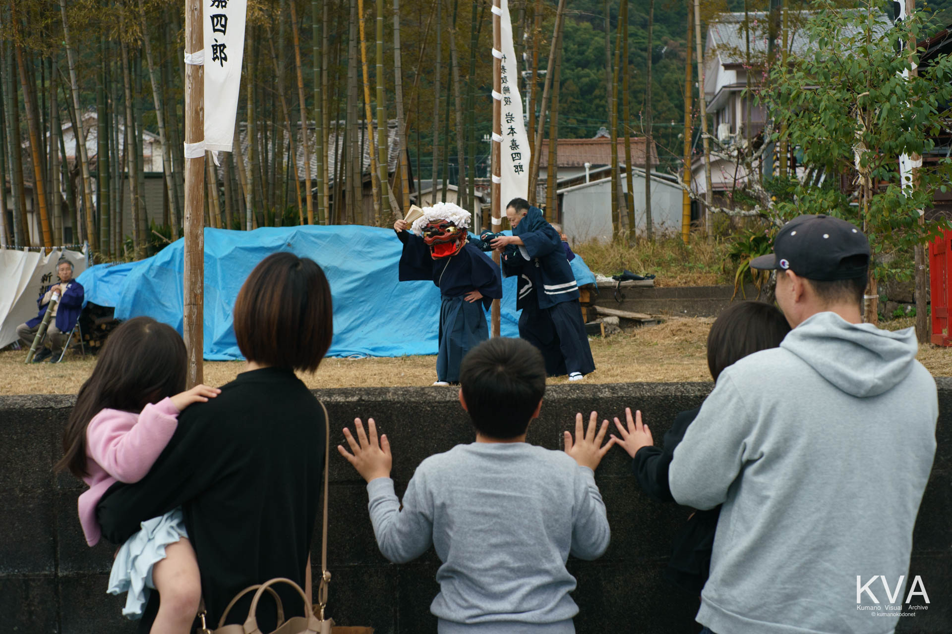 ブロック塀から獅子舞を見つめる子供たち