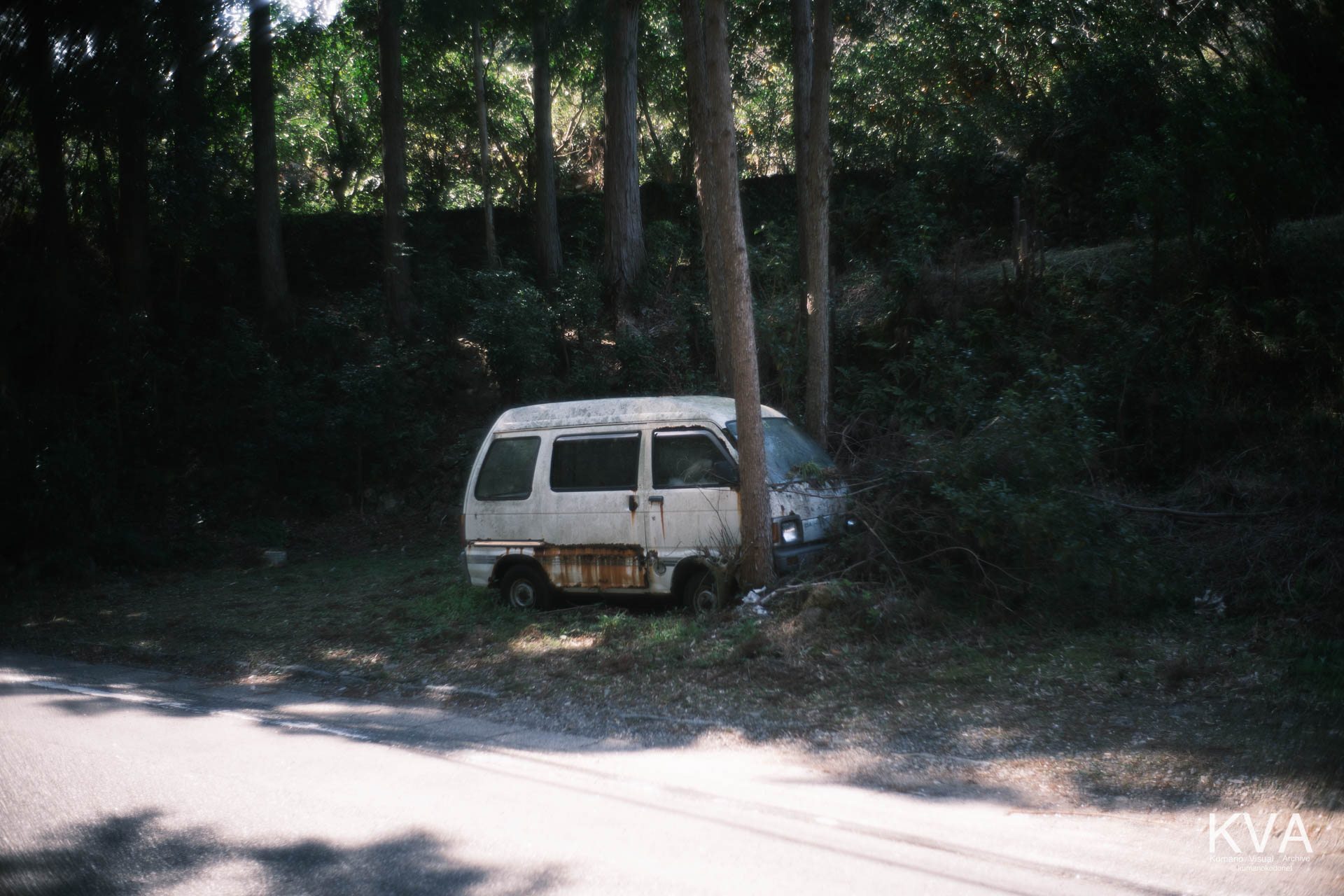 三重県道740号沿い、北桧杖のクマノザクラ手前に佇む「草ヒロ（草むらのヒーロー）」。木々に侵食され、錆に覆われた軽バンが、この地の穏やかな時の積層を物語る。三重県紀宝町北桧杖にて。 ｜ Abandoned Van (Kusahiro) ｜ GFX Classic Neg. ｜ 2026