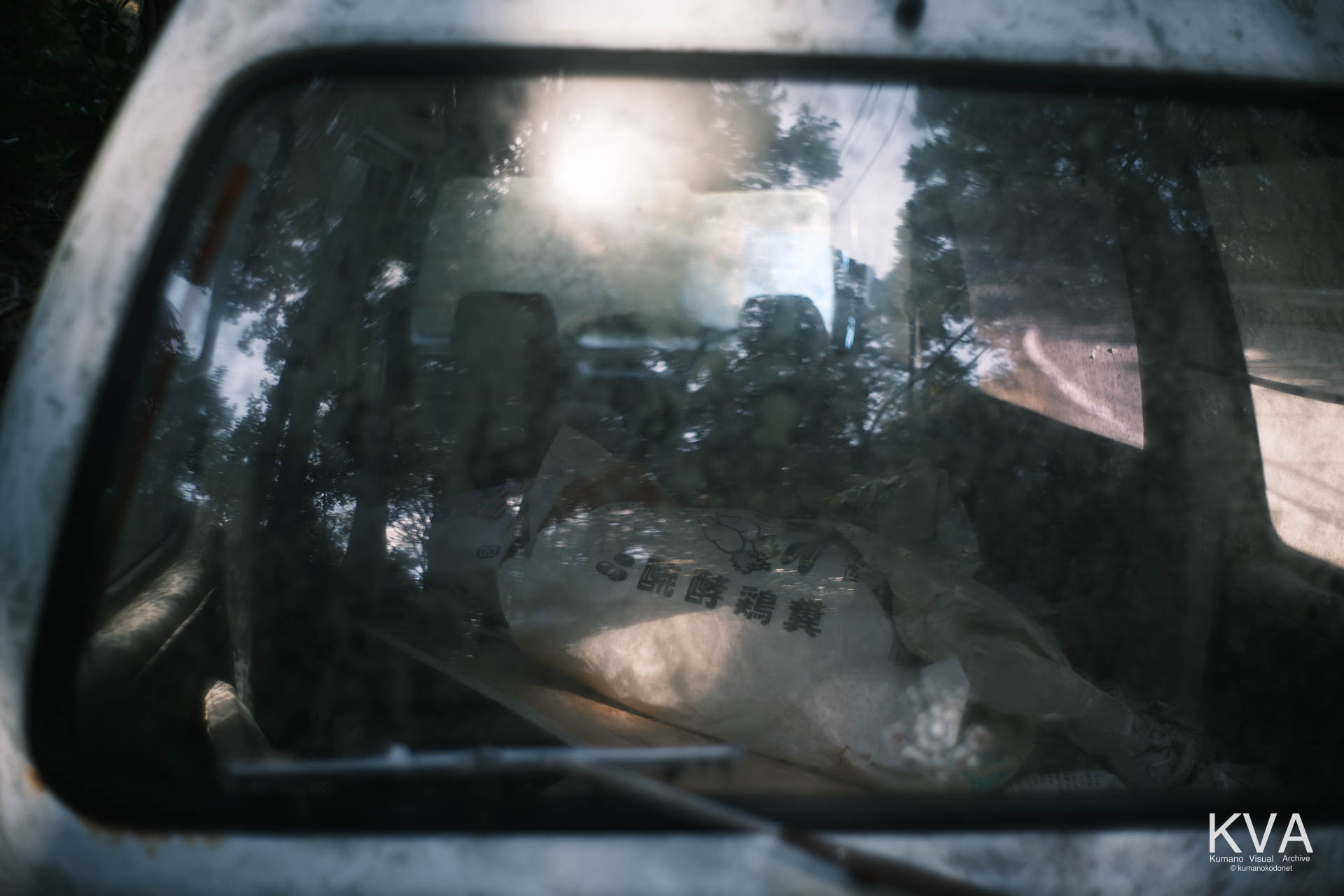 草ヒロとなった軽バンの車内。リアガラス越しに見えるのは、かつて農作業に使われていたであろう「発酵鶏糞」の袋。生活の痕跡がそのまま風化していく、北桧杖の静かな日常。三重県紀宝町北桧杖にて。 ｜ Kusahiro Interior Detail ｜ GFX Classic Neg. ｜ 2026