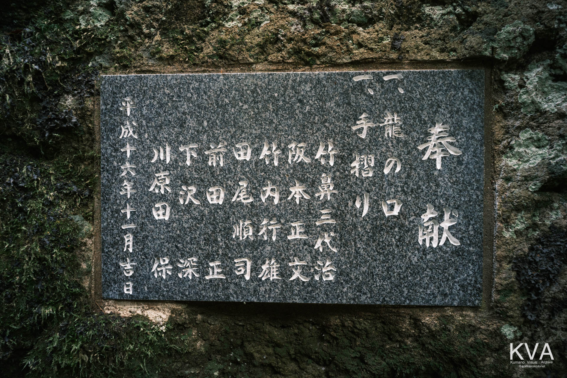 手水舎横の岩壁に設置された龍の口と手摺りの奉献銘板