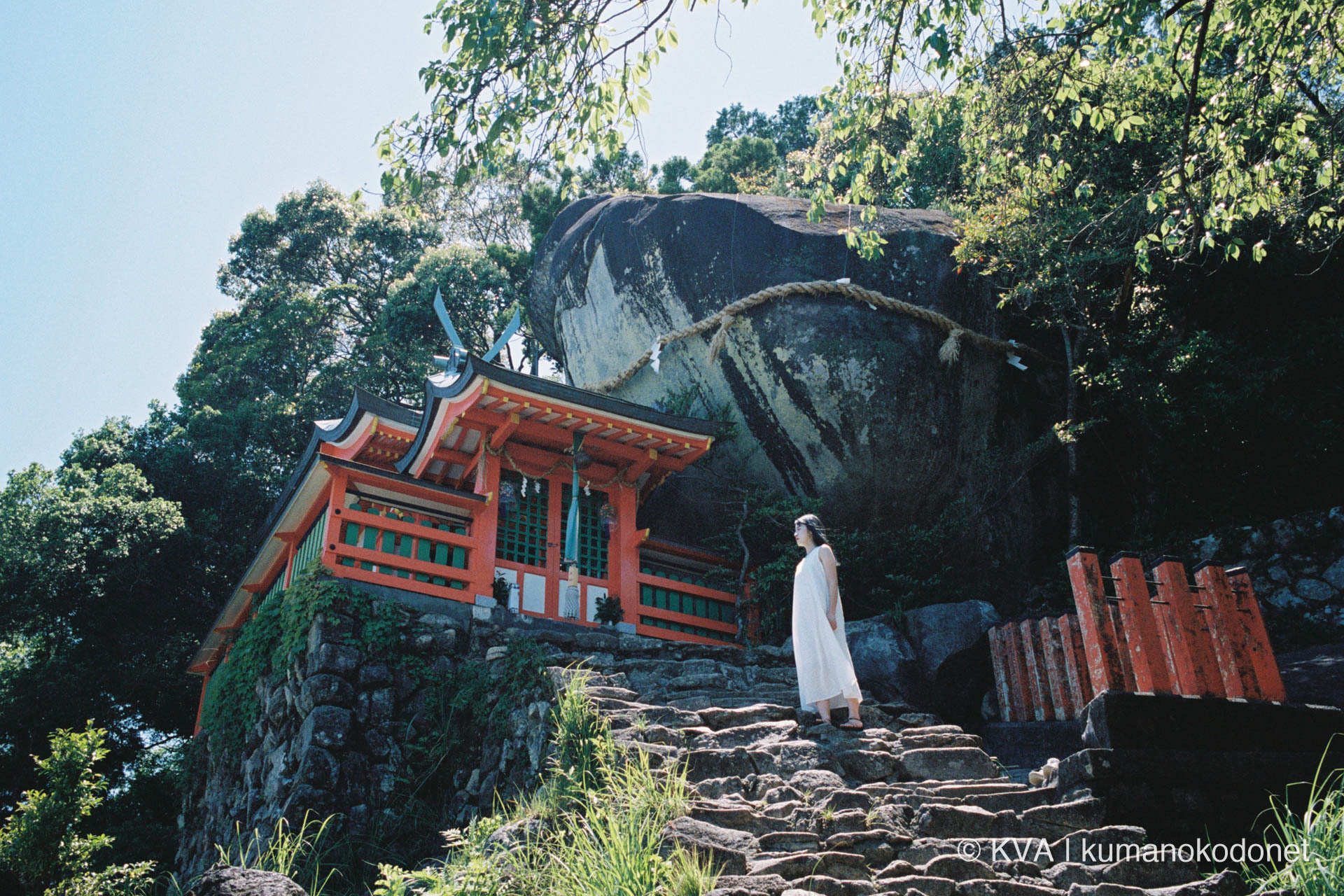 和歌山県新宮市の神倉神社に鎮座する巨岩「ゴトビキ岩」と、朱塗りの社殿の傍らに佇む女性をKodak PORTRA 400で捉えたフィルムポートレート