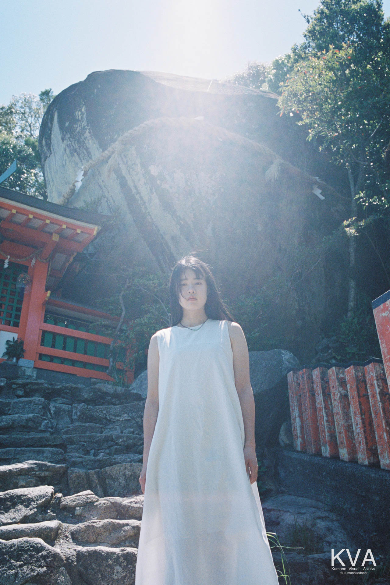 新宮市の神倉神社にそびえるゴトビキ岩の前に、Kodak PORTRA 400の柔らかな光に包まれて立つ白いワンピースの女性のフィルムポートレート