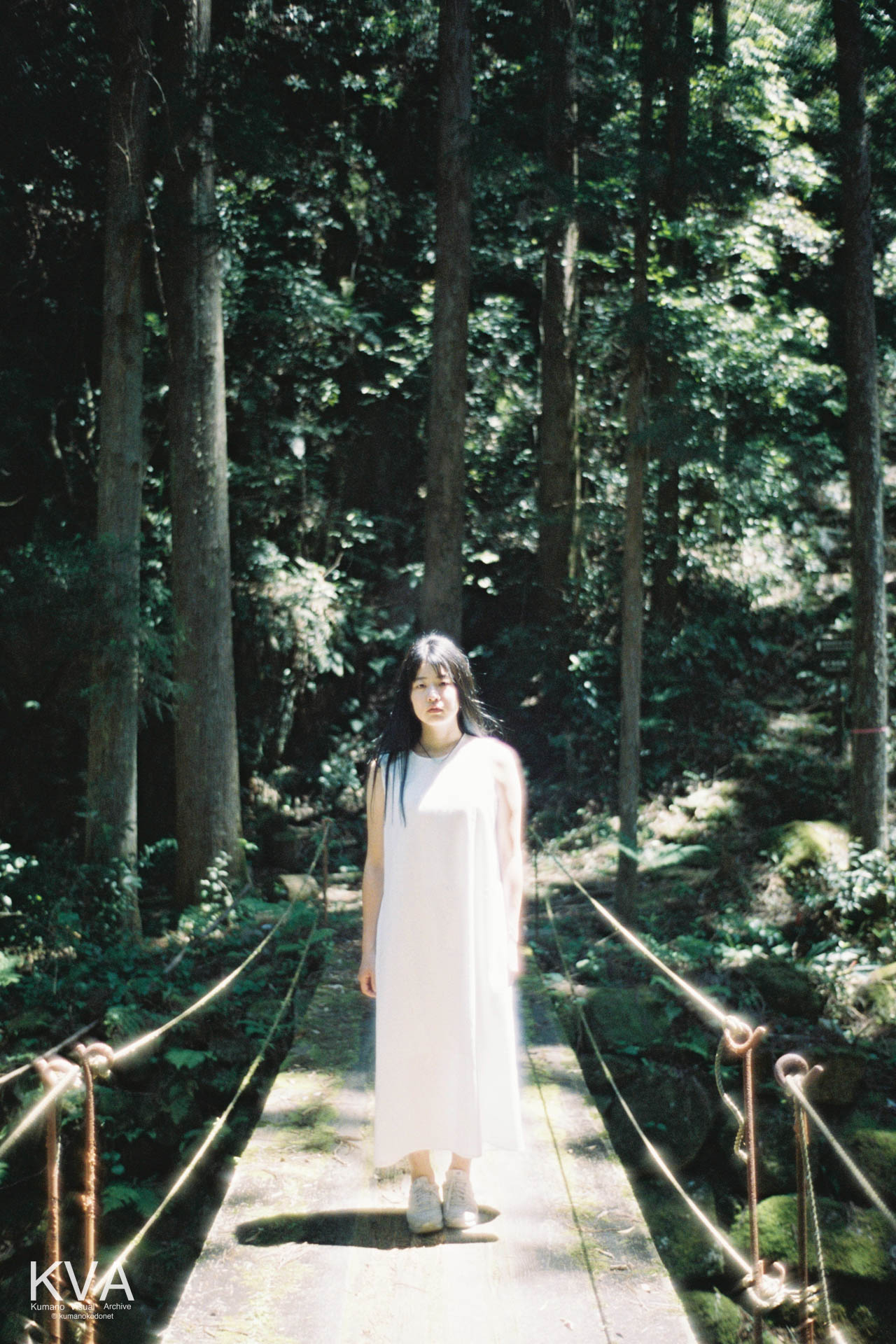 桑の木谷川に架かる橋の上にまっすぐ立ち、正面を見つめる女性のポートレート