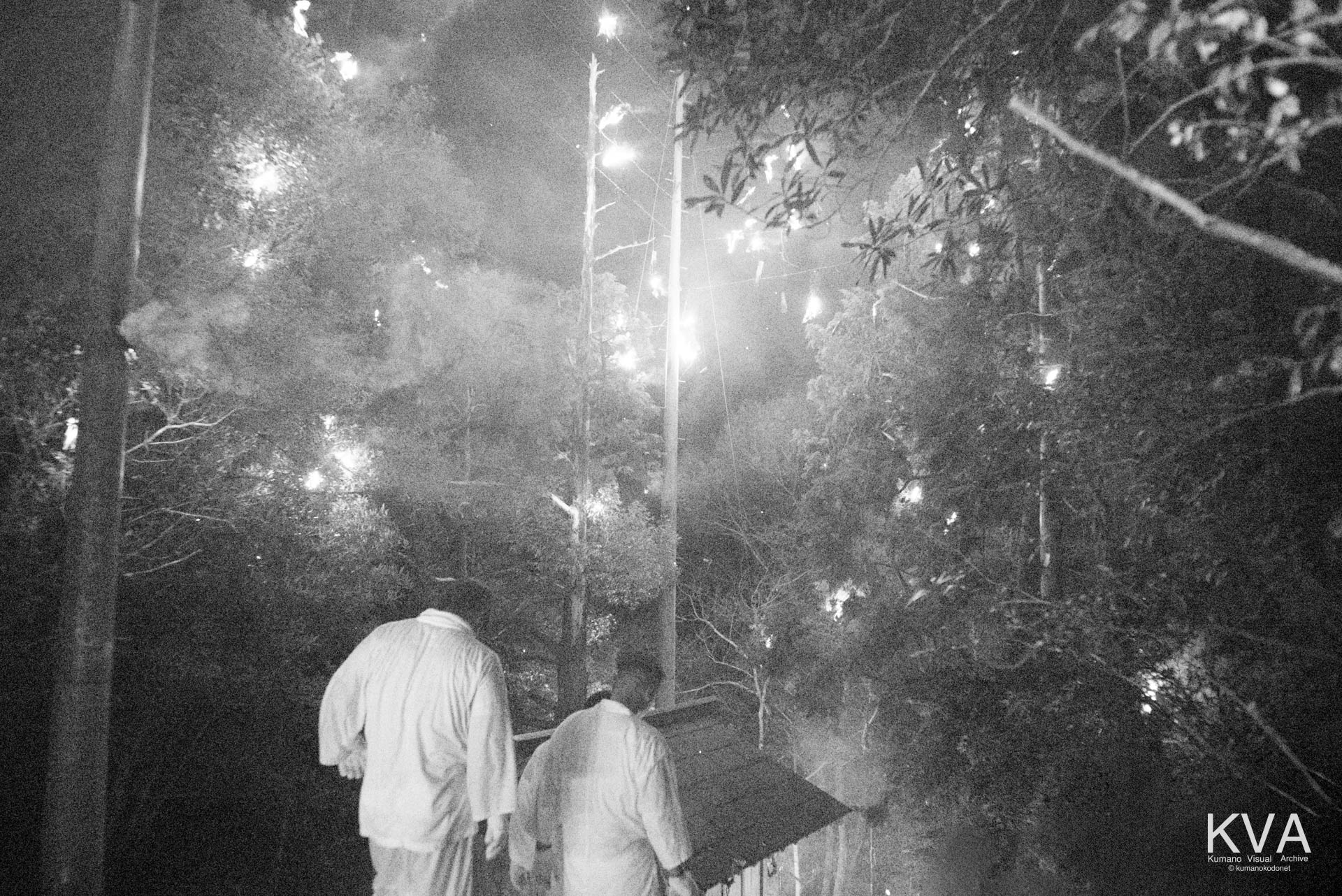 頭上に残火が残る裏山から神事を終えて下山する参加者たち