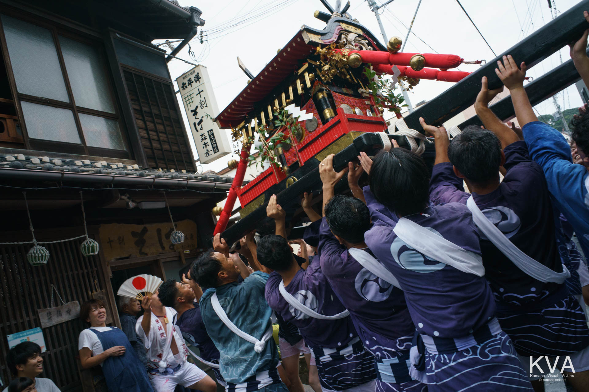 渡御の途中で店舗の軒先に神輿を高く差し上げる担ぎ手たち