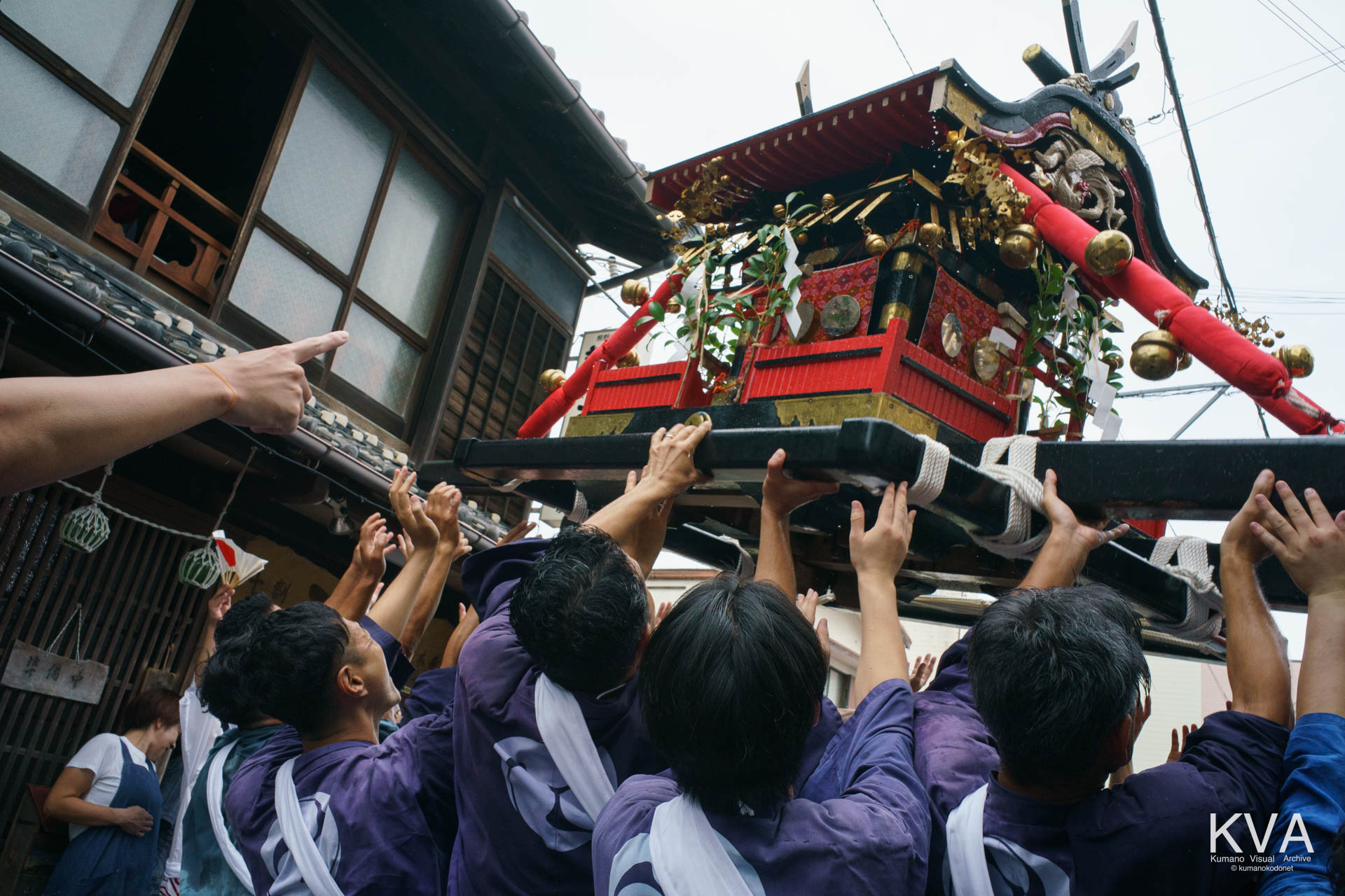 沿道のそば店前で神輿を正面に高く掲げて練る担ぎ手たち
