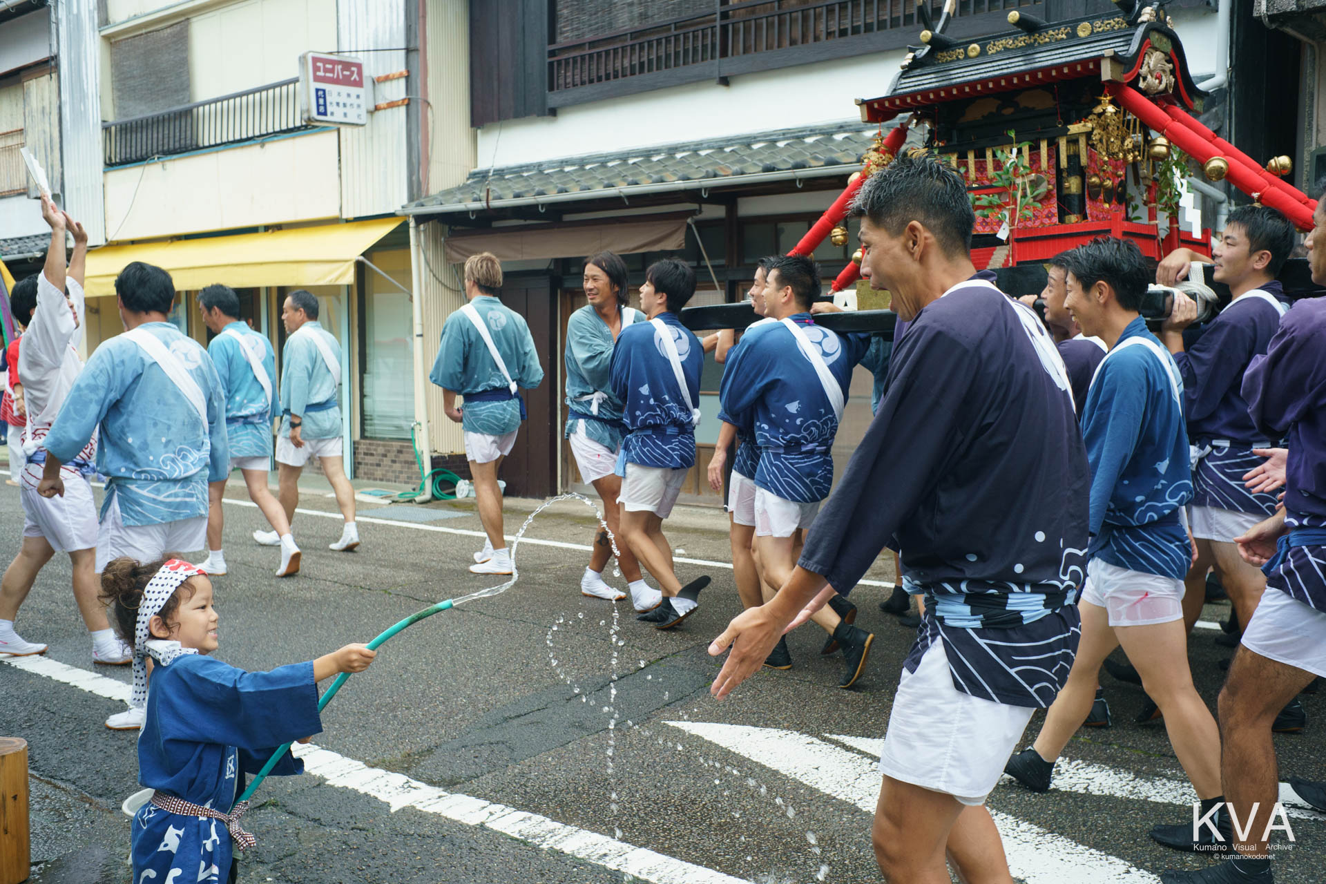 沿道で水をかける子供と笑顔で応える担ぎ手たち
