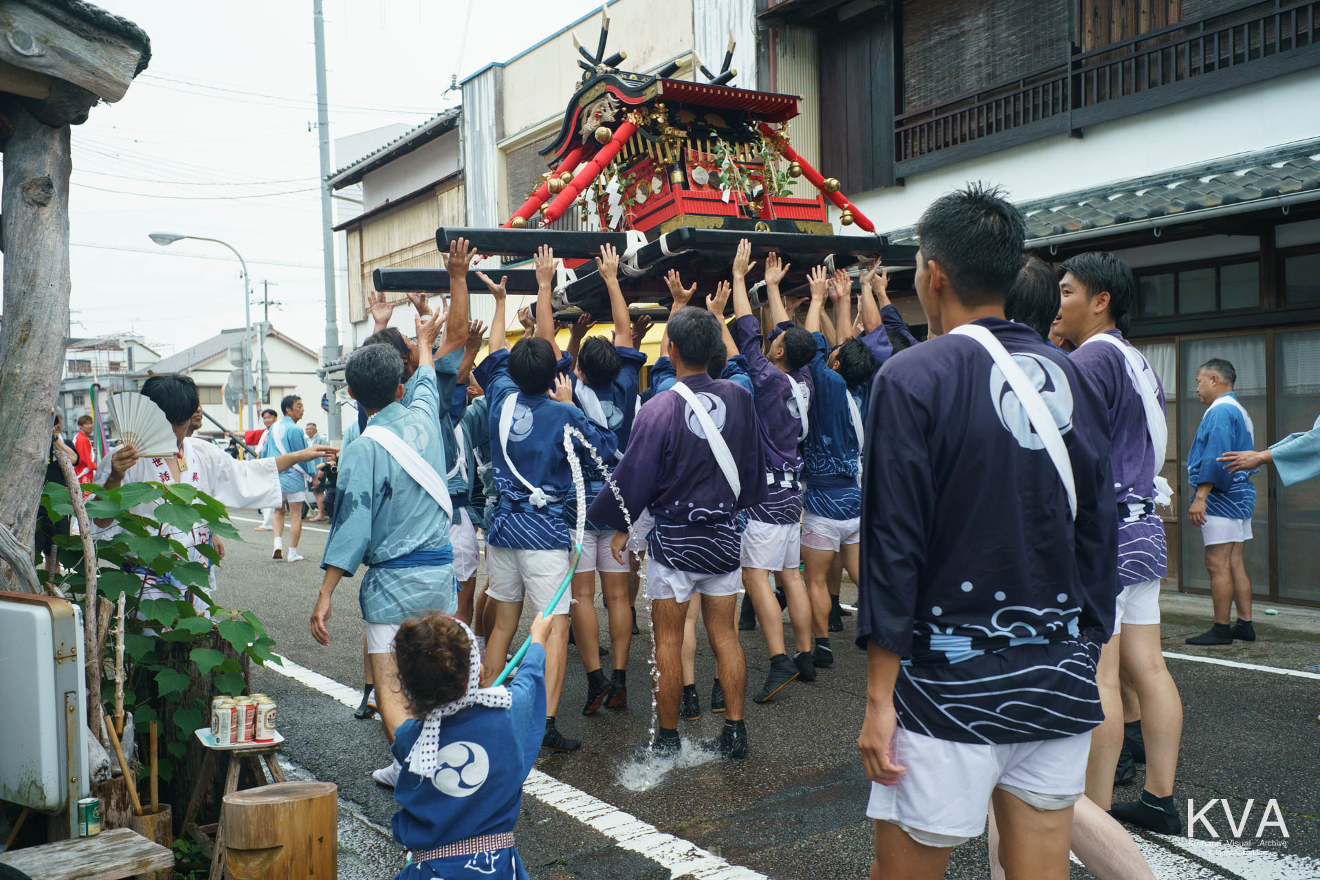水がかかるなか町中で神輿を高く差し上げる担ぎ手たち